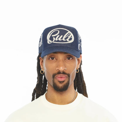 Ballers Clothing Shop blue denim mesh back trucker hat with white Cult embroidery worn by a man