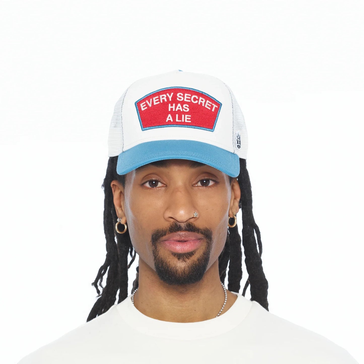 Ballers Clothing Shop white and blue mesh trucker hat with Every Secret Has A Lie red patch worn by a man