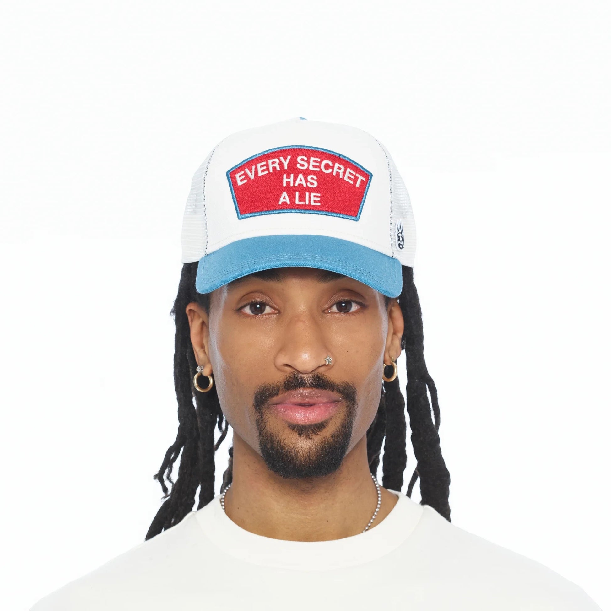 Ballers Clothing Shop white and blue mesh trucker hat with Every Secret Has A Lie red patch worn by a man
