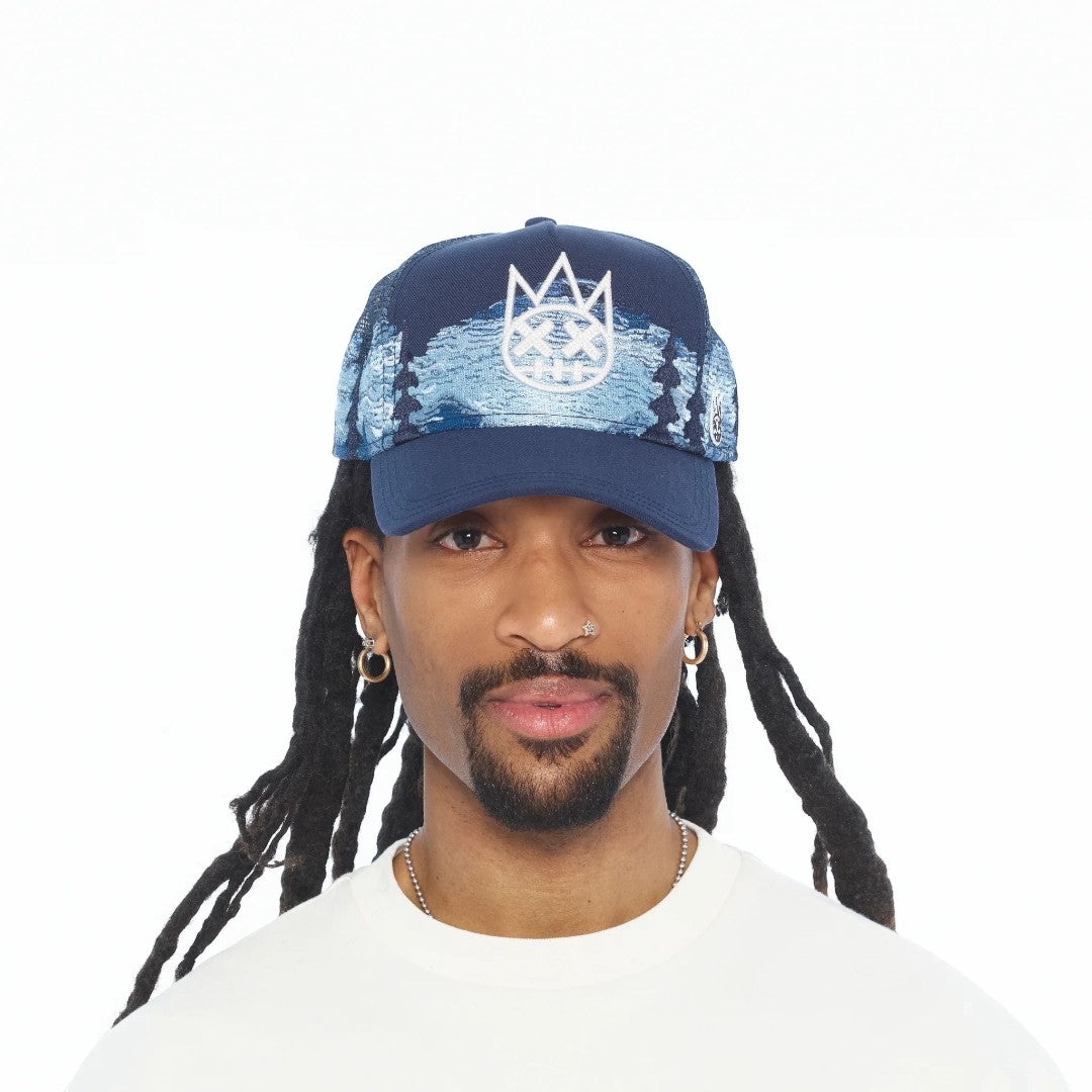 Ballers Clothing Shop navy blue trucker hat with white mountain graphic and crown logo worn by a man with dreadlocks